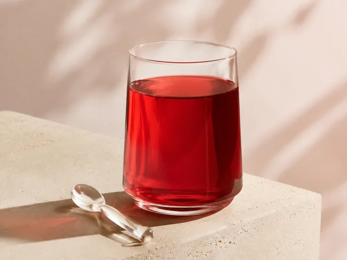 Ein Glas mit rotem Getränk auf einem hellen Steinquader im Sonnenlicht